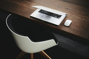 Witte stoel en half dichtgeklapte laptop op houten bureau